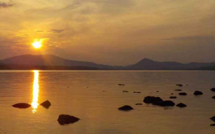 rocks poke out of still water as the sun sets behinds mountains in maine